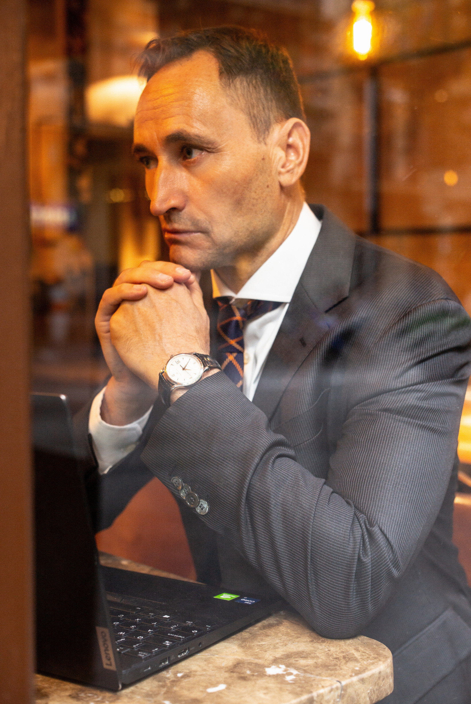 John-Oliver Breckoff in a suit, listening attentively at a table with his laptop