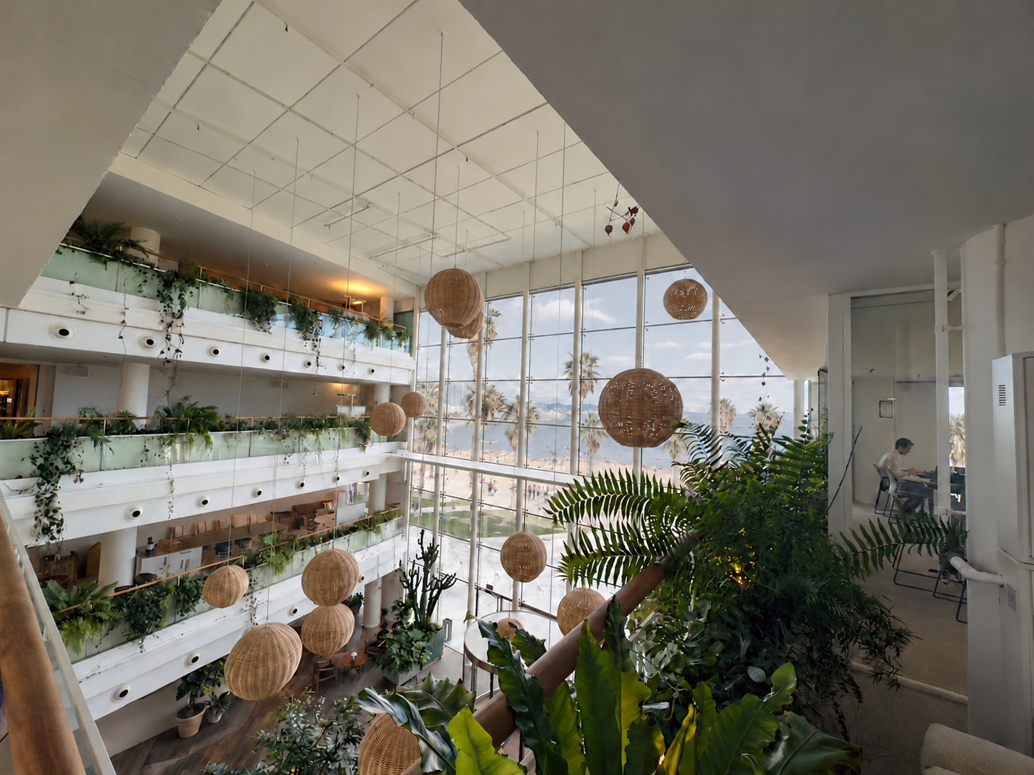 Norrsken House Barcelona: a planted atrium overlooking the Mediterranean, with a person working in the office on the right